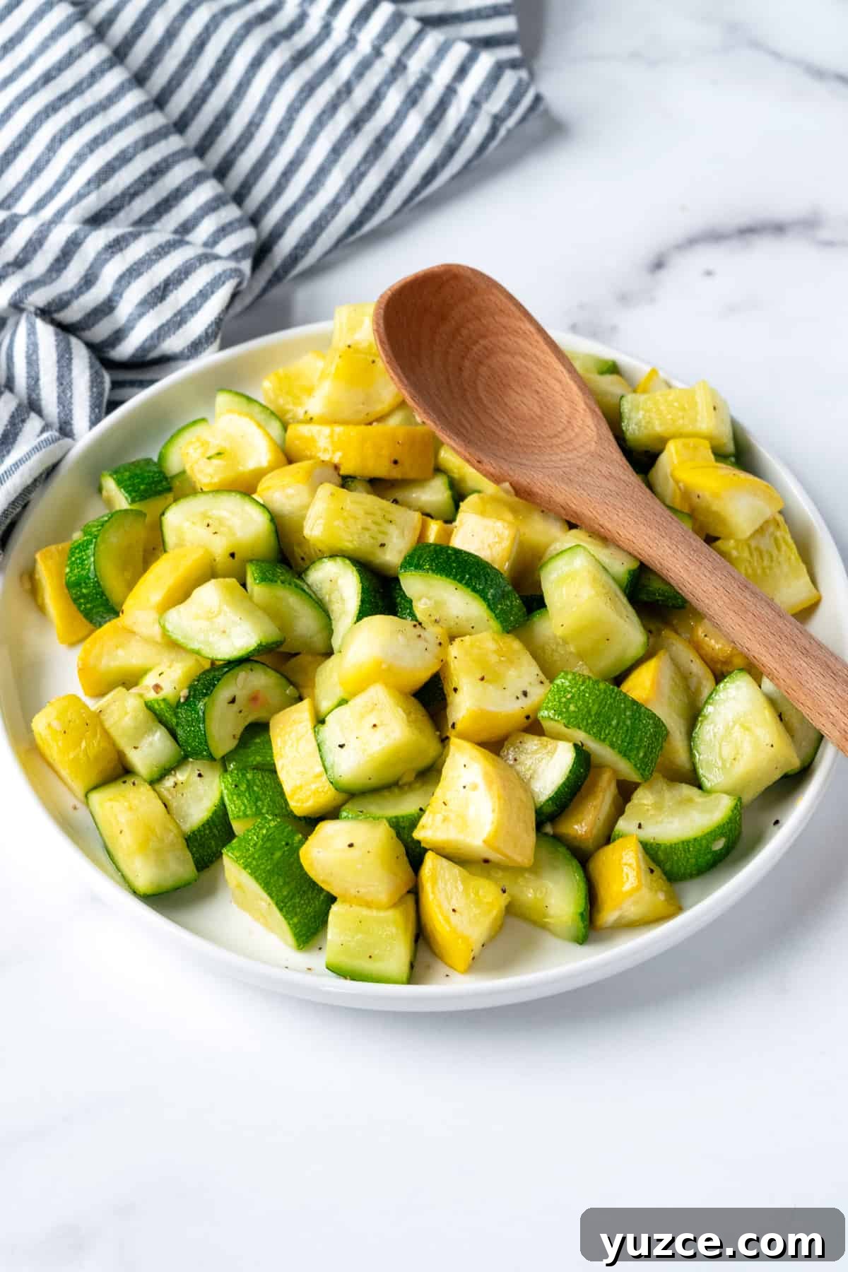 Crispy Air Fryer Zucchini & Summer Squash Recipe 7 Cooked Zucchini and Squash slices on a white plate with a serving spoon.