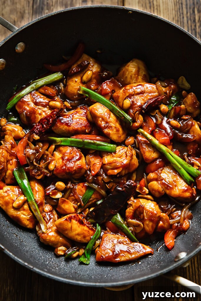 Sichuan Szechuan Chicken: Spicy Stir-Fry Recipe with Garlic Chili Oil 3 Top down shot of szechuan chicken in a large pan stir fried with green onions and red peppers, topped with peanuts
