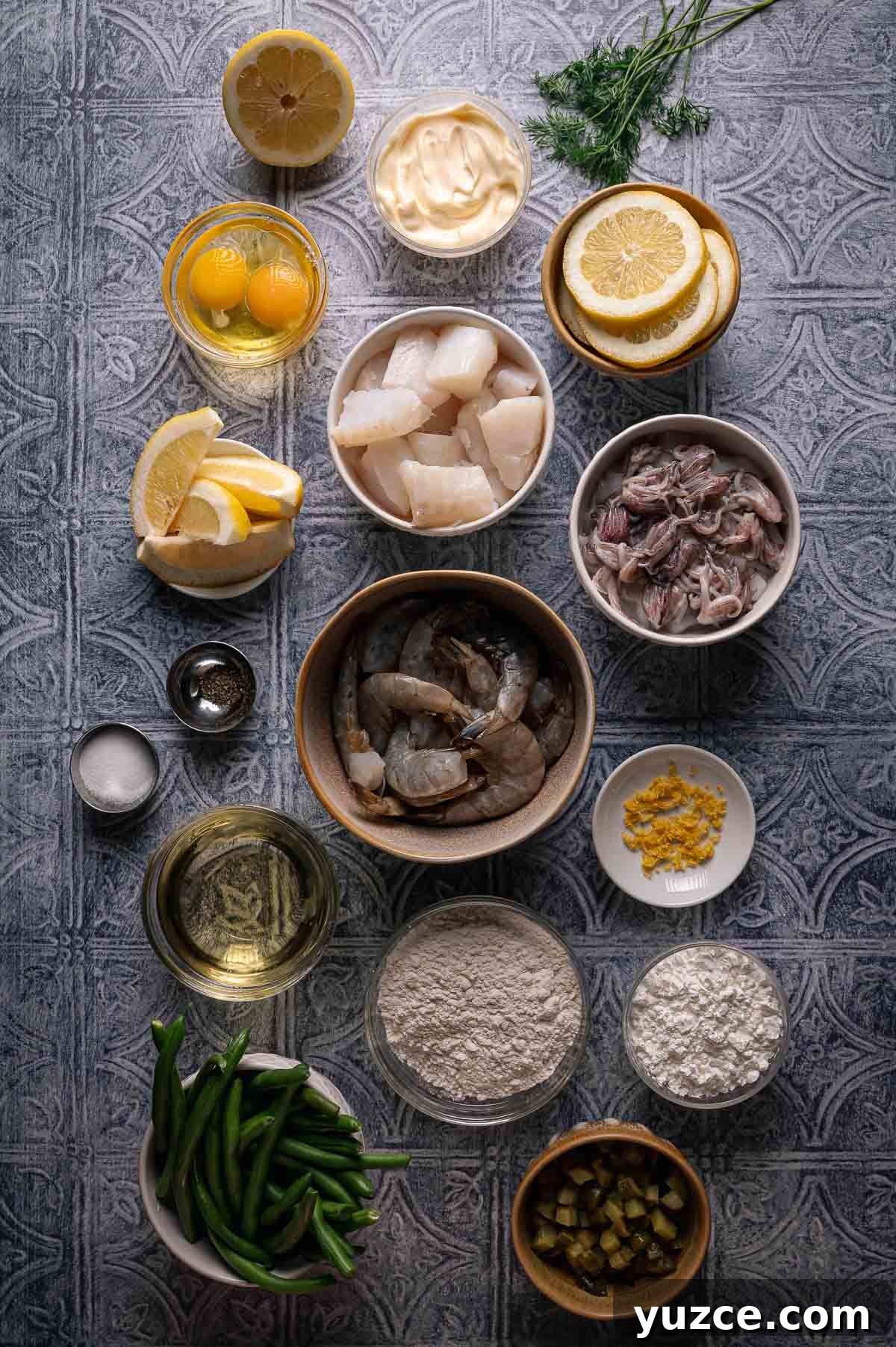 Crispy Fritto Misto with Lemon-Dill Tartar Sauce 3 Various ingredients for a fritto misto seafood dish are arranged on a patterned surface, including shrimp, cod, eggs, flour, lemon, green beans, mayonnaise, and seasonings.