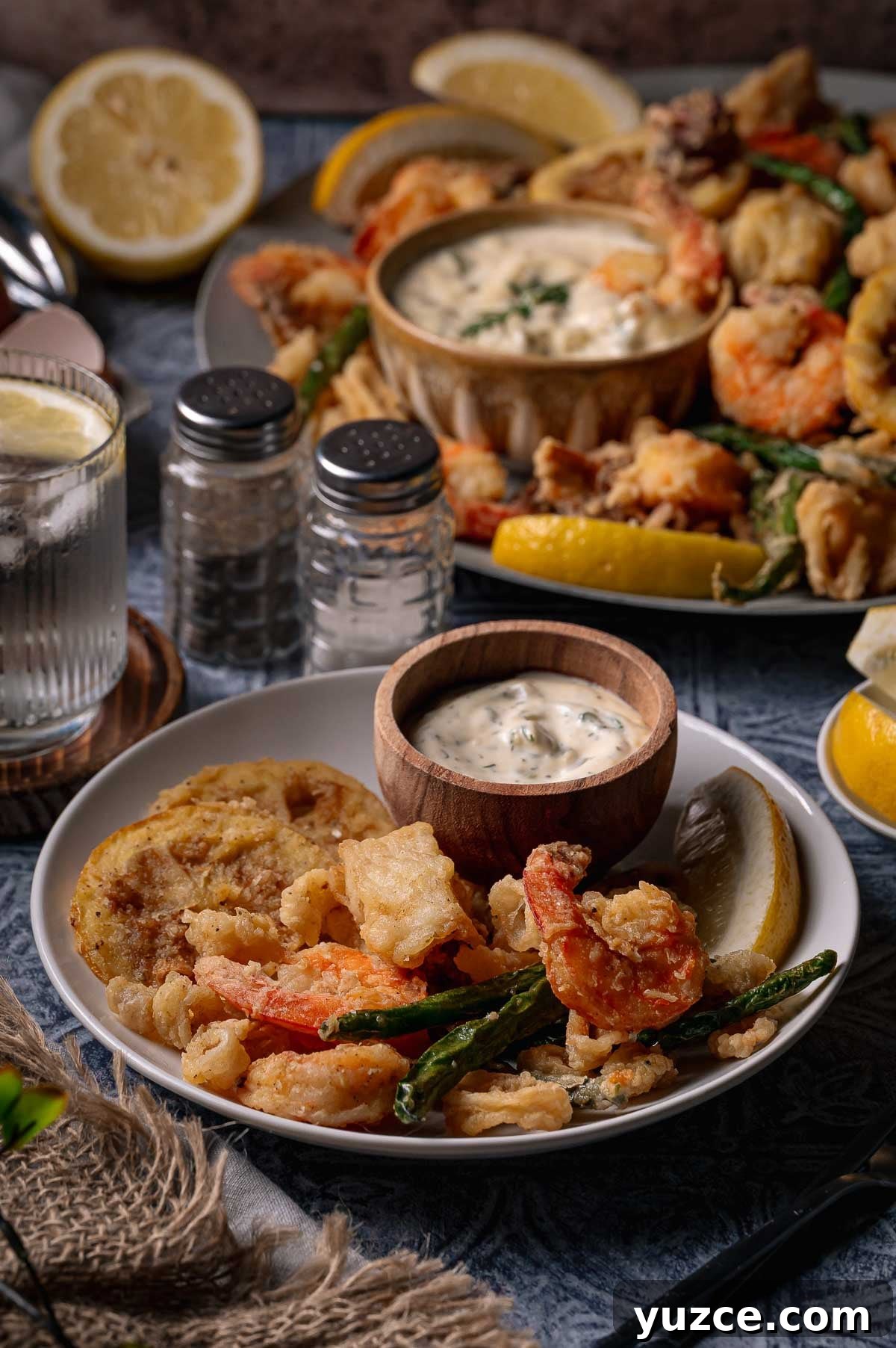 Crispy Fritto Misto with Lemon-Dill Tartar Sauce 5 A plate of fritto misto; fried seafood and vegetables with a lemon wedge and dipping sauce, accompanied by a glass of water and condiments.