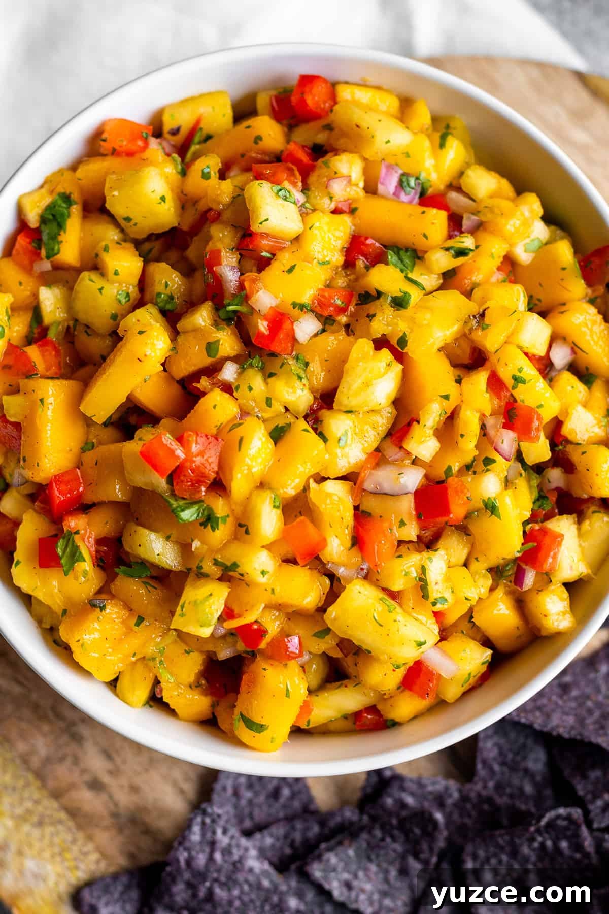 White bowl with mango pineapple salsa on a wooden board with blue corn tortilla chips.