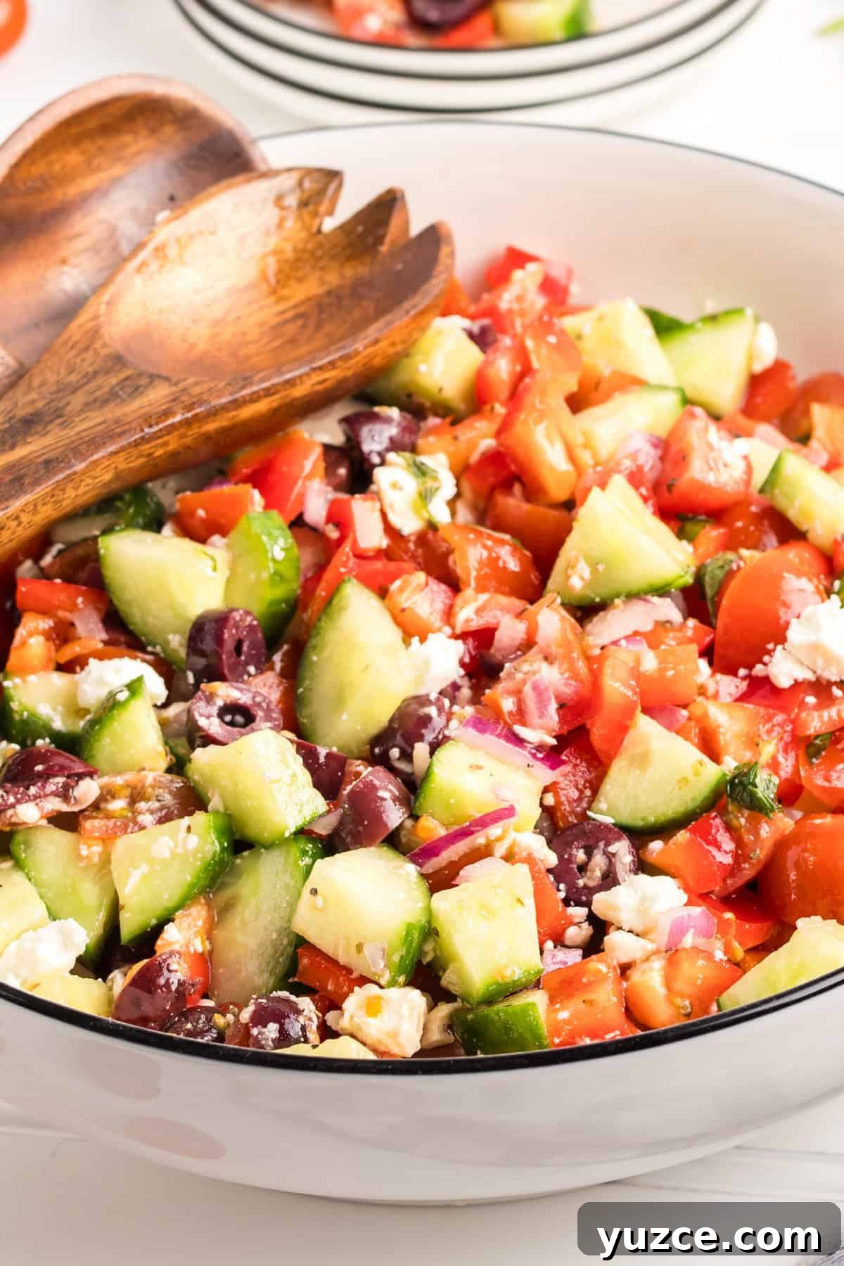 A large bowl filled with Greek salad, showcasing chopped cucumbers, cherry tomatoes, red bell peppers, kalamata olives, red onion, crumbled feta, and mint.