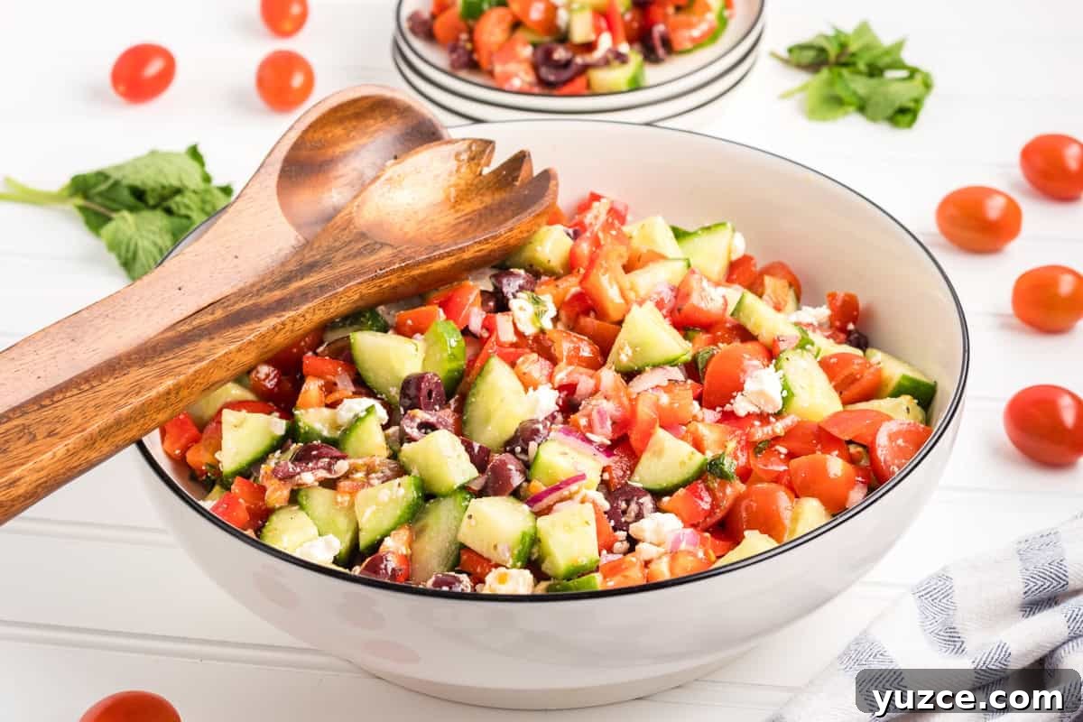 A large bowl of Greek chopped salad with wooden salad servers resting on top.