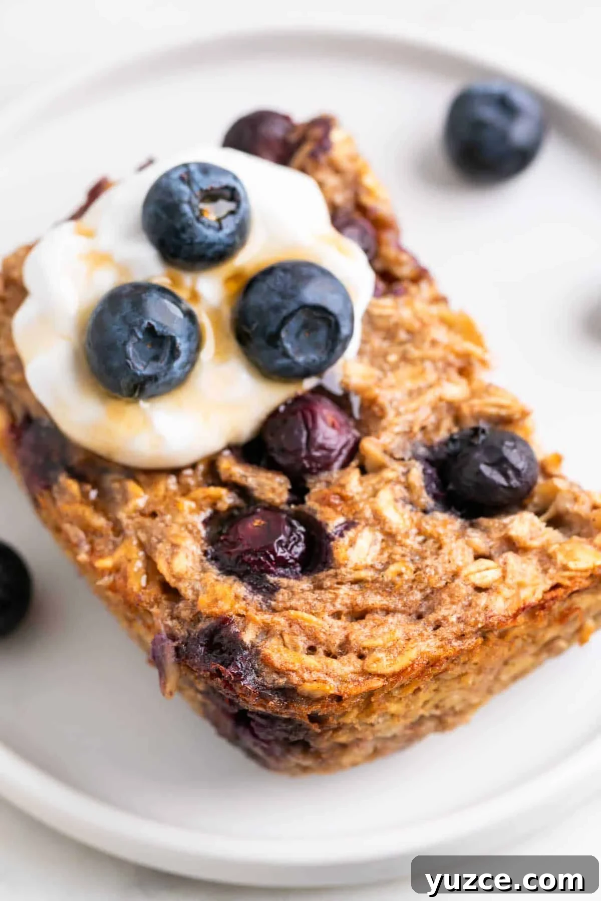 Vegan Baked Oatmeal Recipe with Fruit and Nuts 11 Slice of vegan baked oatmeal served on a plate with blueberries.