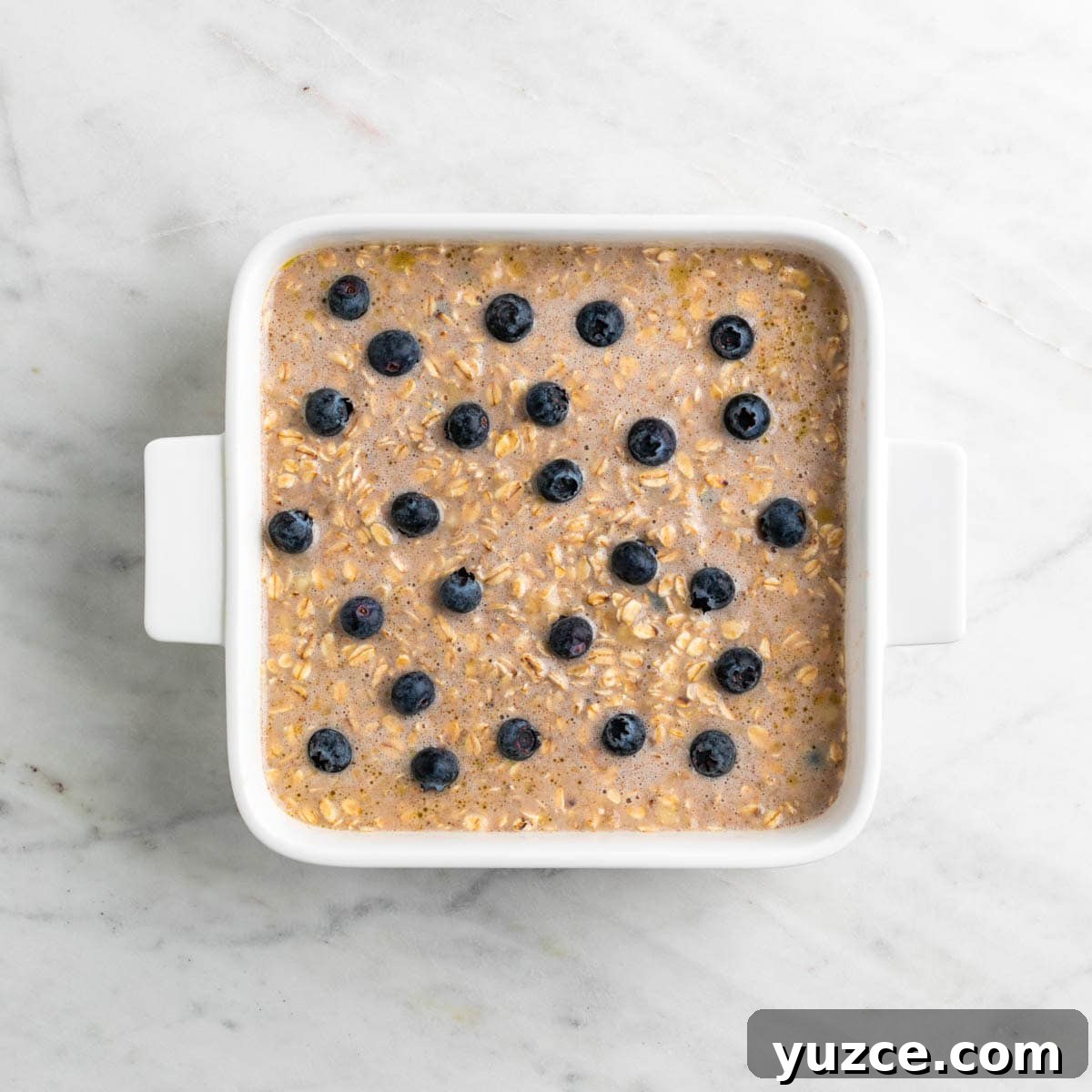 Vegan Baked Oatmeal Recipe with Fruit and Nuts 7 Vegan baked oatmeal mixture in a baking dish topped with blueberries.