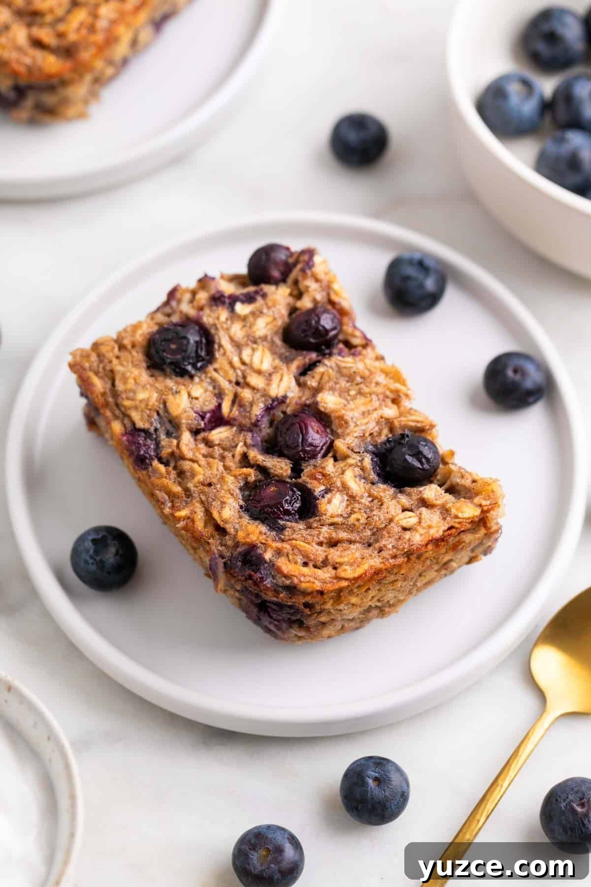 Vegan Baked Oatmeal Recipe with Fruit and Nuts 10 Slice of vegan baked oatmeal served on a plate with blueberries and a spoon.