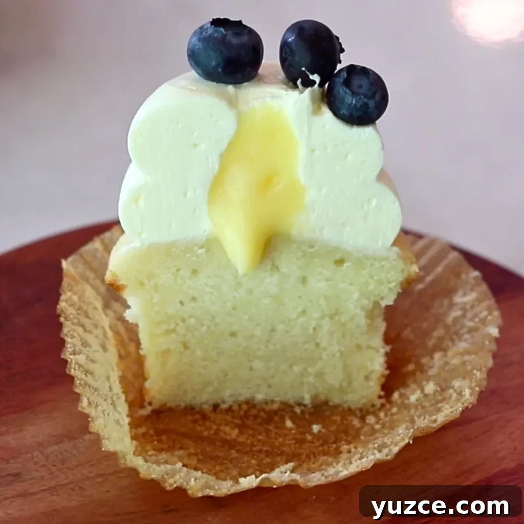 Luscious Lemon Buttercream Frosting Recipe for Cakes and Cupcakes 15 a lemon cupcake with lemon frosting and blueberries on top, cut in half