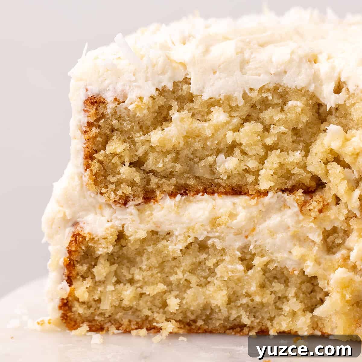 Moist Coconut Layer Cake Recipe 3 front view of a Coconut Cake with a slice cut out of it