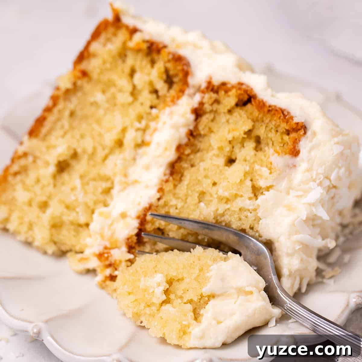Moist Coconut Layer Cake Recipe 18 a fork taking a bite out of a slice of Coconut Cake on a plate