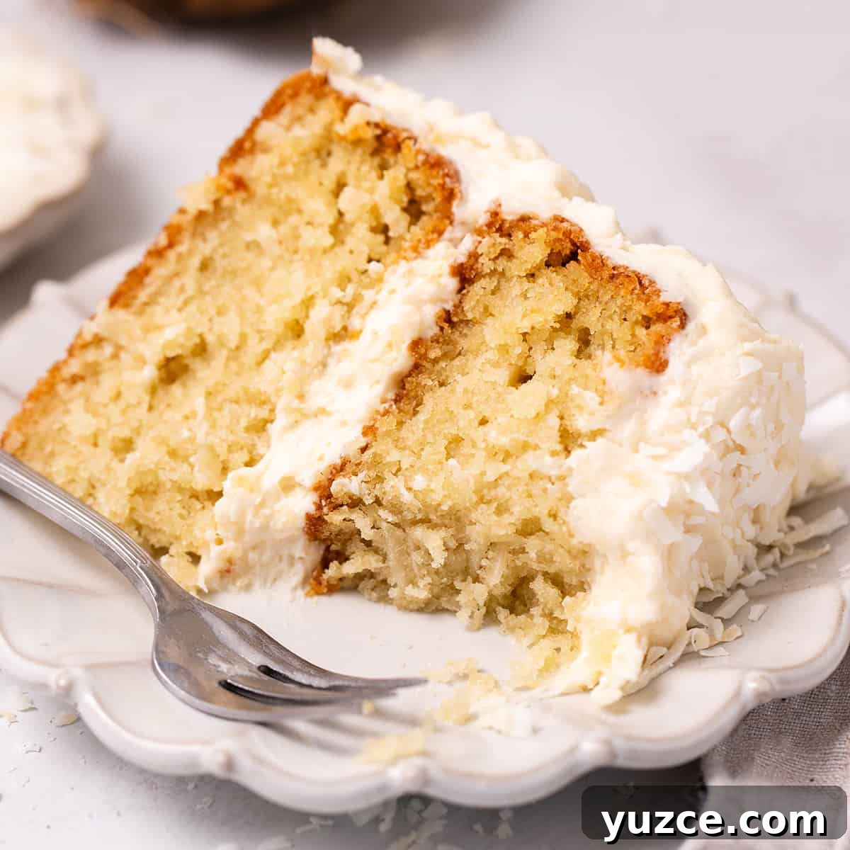 Moist Coconut Layer Cake Recipe 19 a slice of Coconut Cake on a plate with a fork and a bite taken out of it