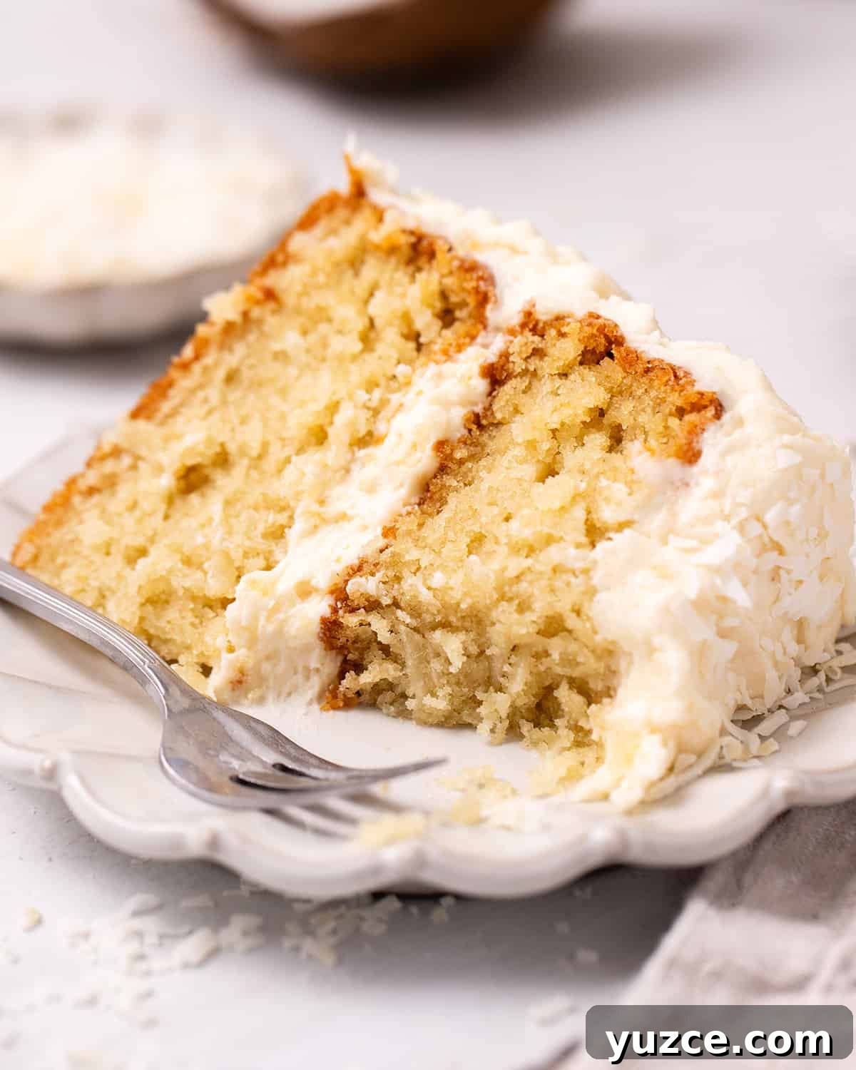 Moist Coconut Layer Cake Recipe 5 a slice of Coconut Cake on a plate with a fork and a bite taken out of it