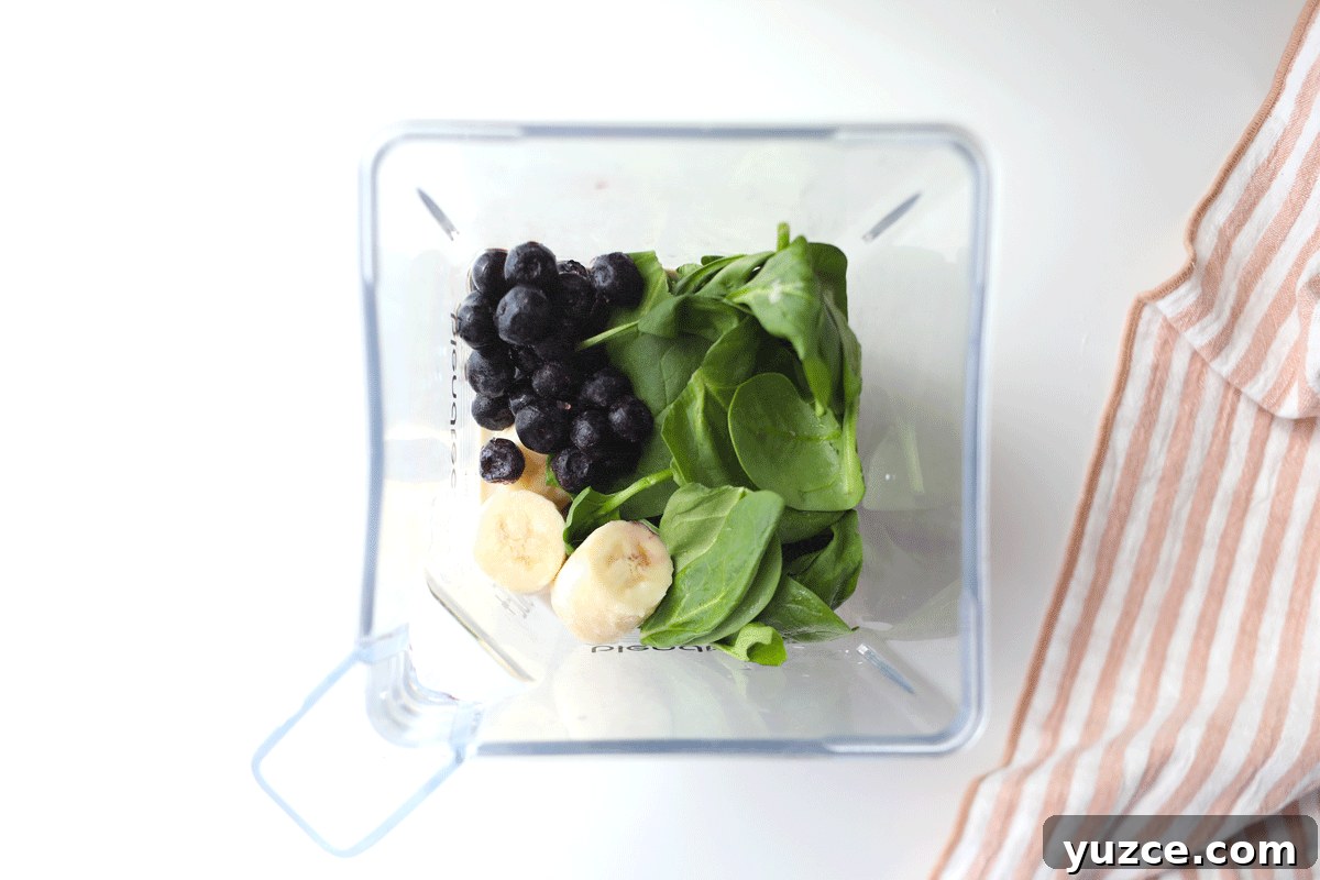 Blueberry Spinach Smoothie Recipe for Energy and Weight Support 4 A blender with frozen blueberries, spinach leaves and bananas in it.