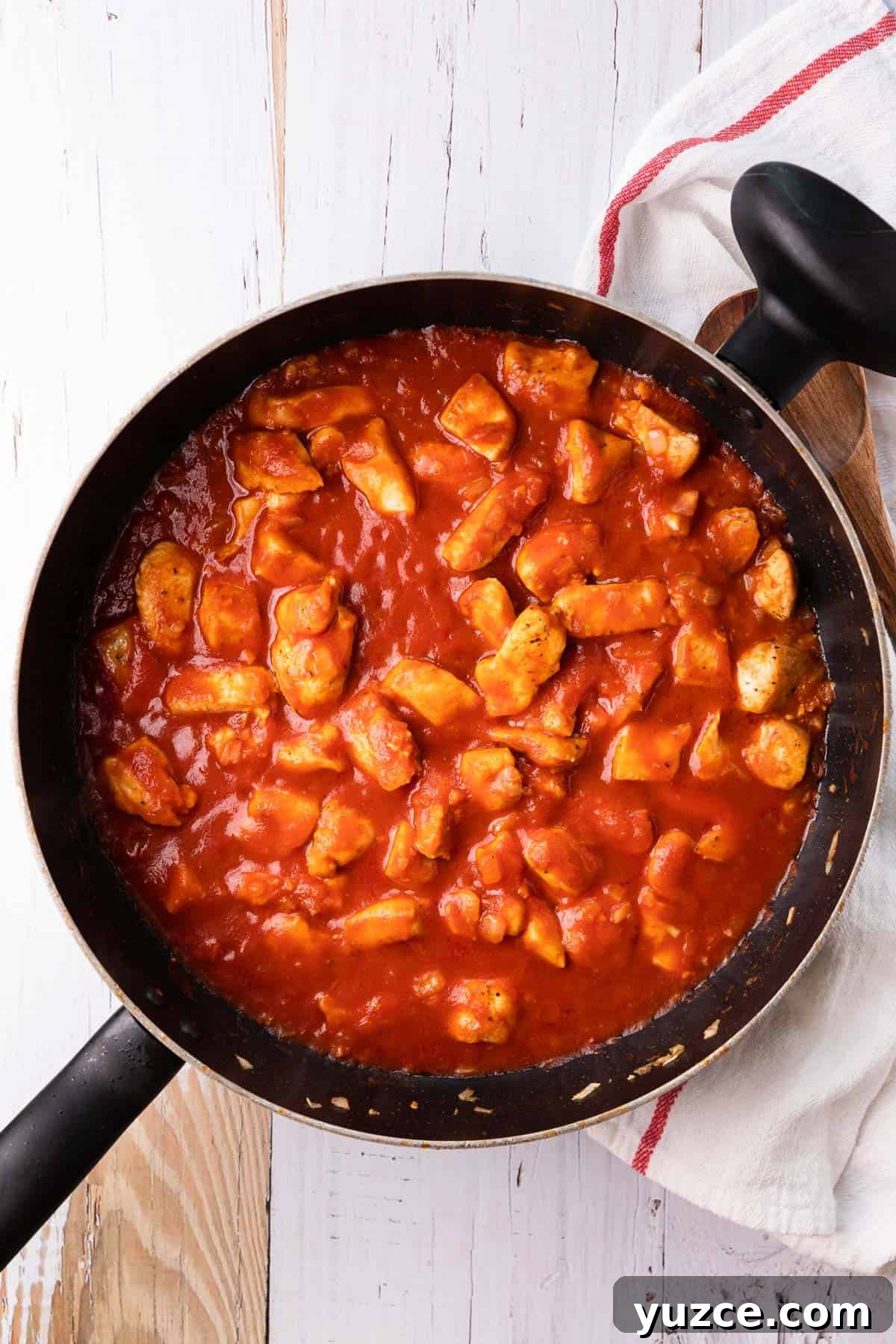 a skillet of chicken pieces cooking in a tomato sauce