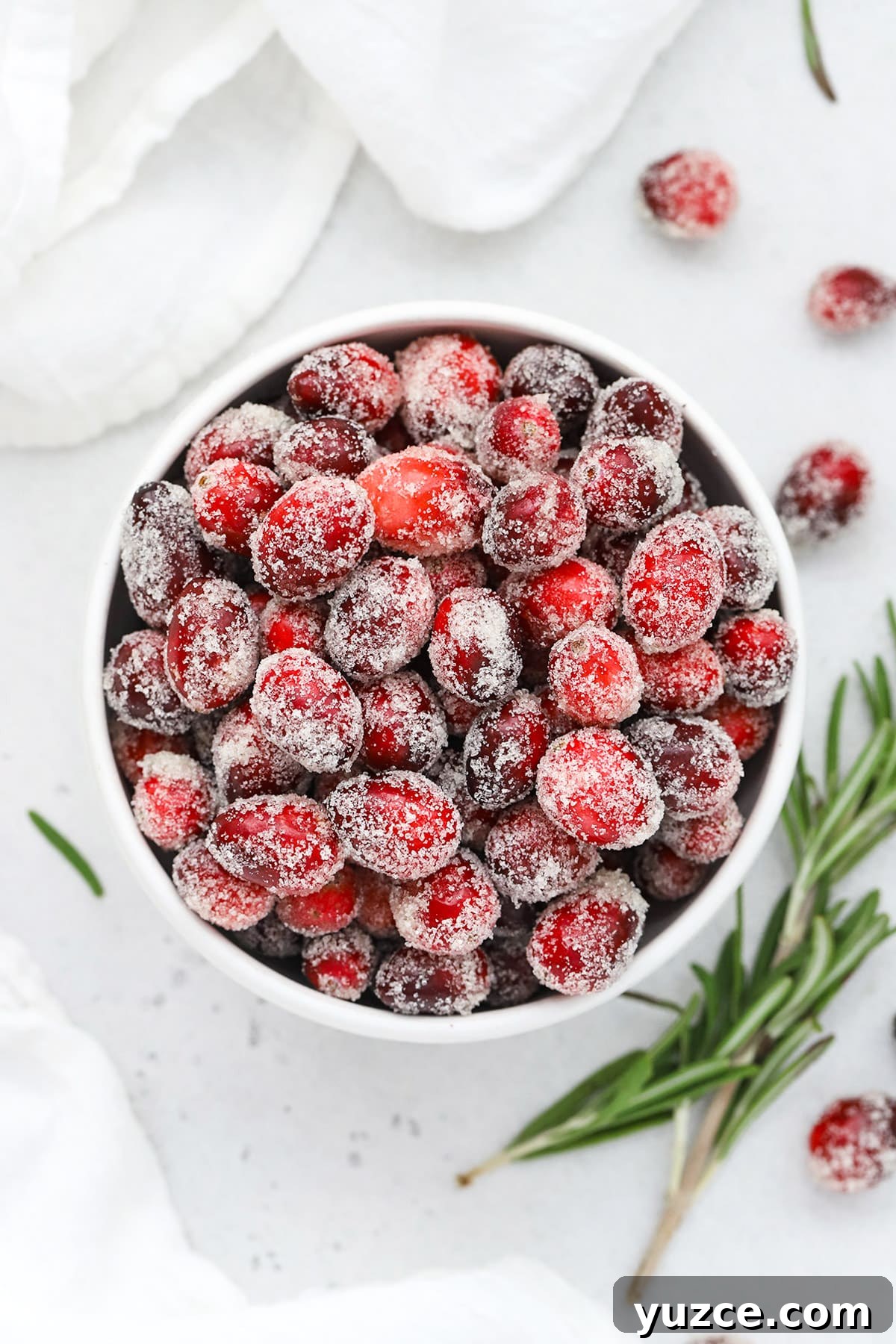 Sugared Cranberries Recipe: Simple Steps for Sparkling Cranberry Garnish 2 Overhead view of a bowl of sugared cranberries with a sprig of rosemary in the background
