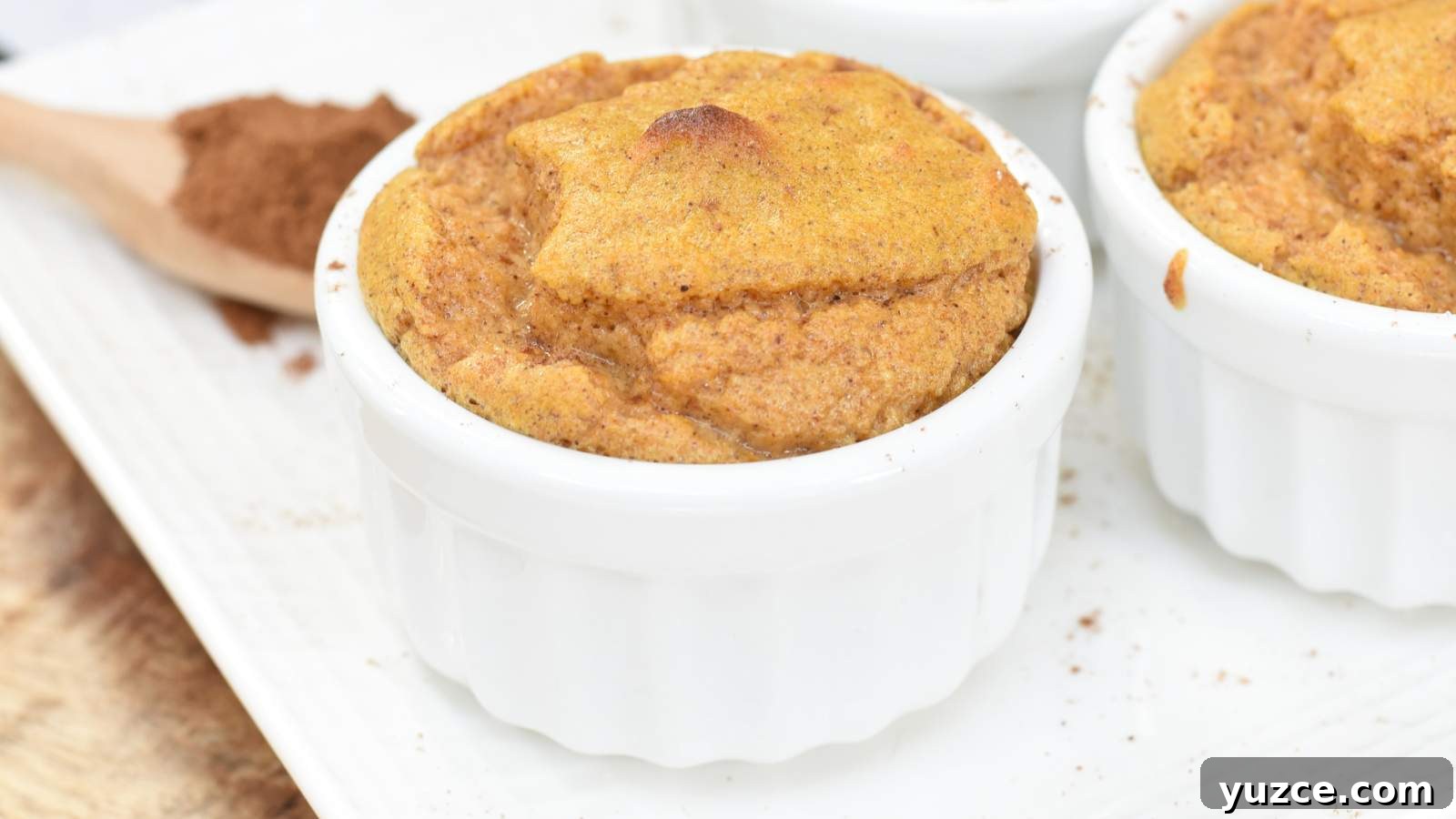 13 Sugar-Free Christmas Sweets That Still Feel Decadent 3 A baked soufflé in a white ramekin sits on a white plate with a wooden spoon and ground cinnamon in the background.