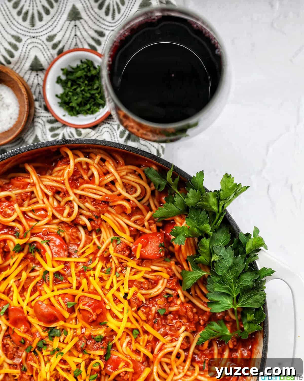 Perfect Wine Pairings for Popular Pasta Dishes 4 Filipino-style spaghetti in a saucepan with glass of red wine and side of salt, pepper, parsley, shredded cheese.