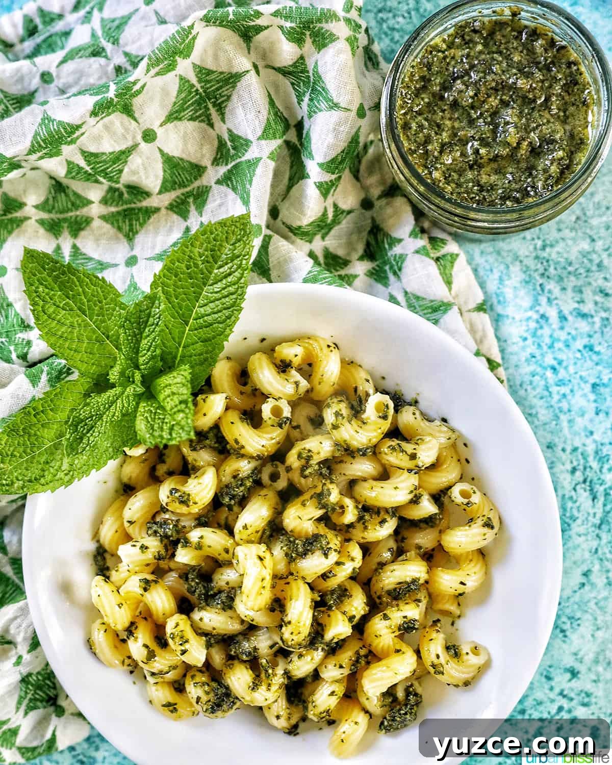 Perfect Wine Pairings for Popular Pasta Dishes 7 pesto pasta in a white bowl on blue background with a side of pesto pasta in a jar.