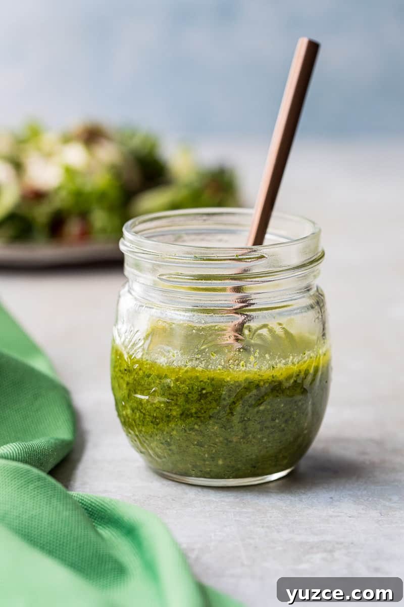 Creamy Pesto Salad Dressing Recipe for Fresh Greens 2 jar of pesto salad dressing with spoon in it next to green napkin and in front of plate with salad on it.