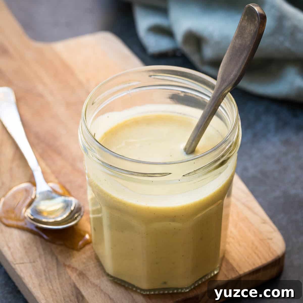 jar of healthy honey mustard salad dressing on a cutting board with spoonful of honey next to it