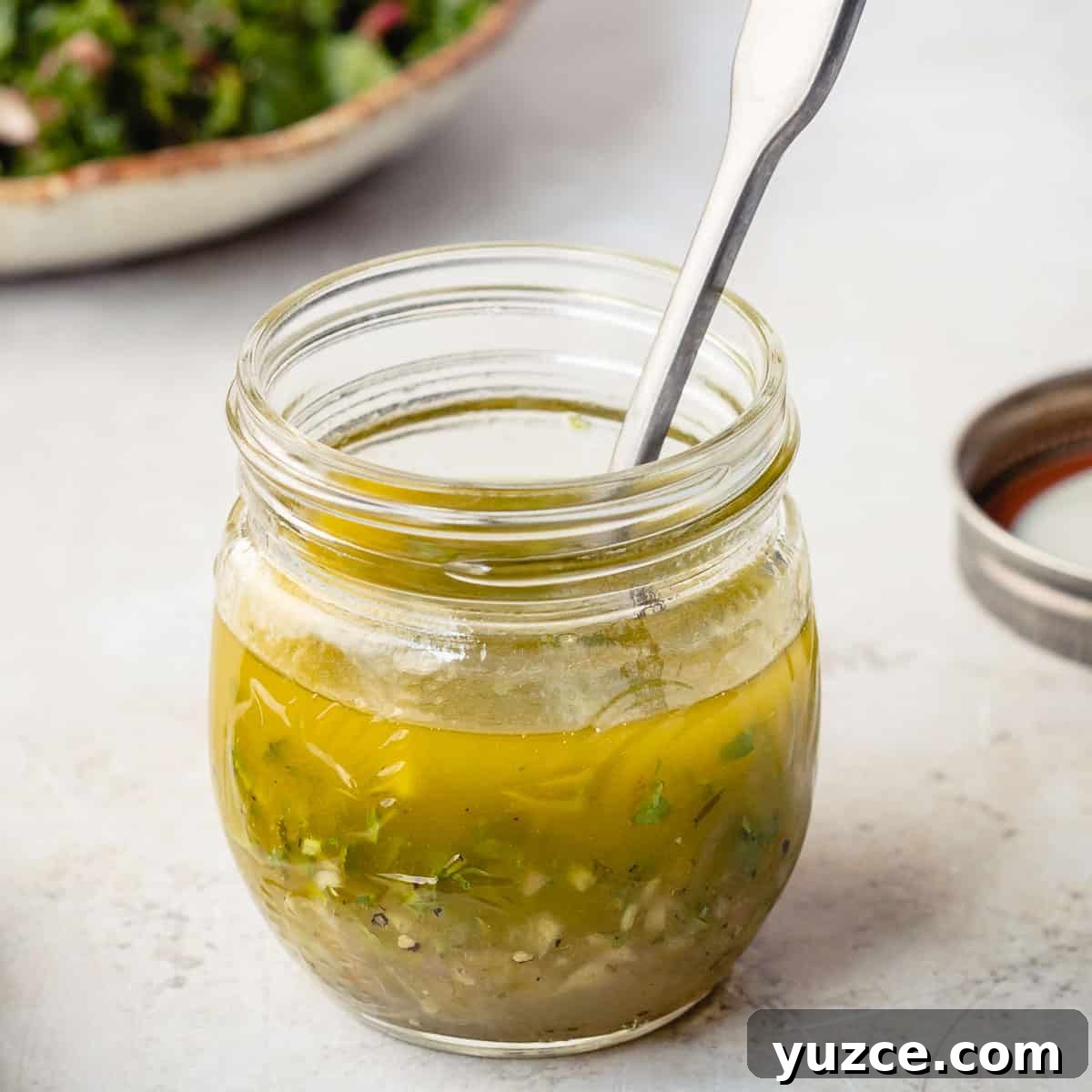 jar of honey lime dressing with spoon in front of salad plate and next to jar lid.